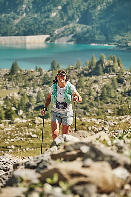 Ines en course sur un trail de montagne, bâtons en main, au-dessus d'un lac